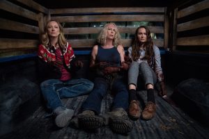 Les trois femmes victimes de Michael Myers, dont Jamie Lee Curtis au milieu, sont assises à l'arrière d'un camion, dans ce qui semble une remorque, l'air exténué ; plan du film Halloween Kills.