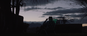 La silhouette de Clint Eastwood, près de son véhicule, se dessine en contre-jour sous un ciel gris de crépuscule dans le film Cry Macho.