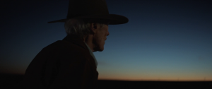 Clint Eastwood regarde l'horizon, chapeau de cow-boy sur le chef, la nuit tombe dans le film Cry Macho.
