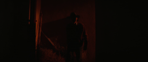 Clint Eastwood dans l'embrasure d'une grange, baignée dans une lumière rouge ; plan issu du film Cry Macho.