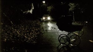 Sur une route de campagne, de nuit, une voiture phares allumés s'approche d'un landau abandonné ; scène du film Dead End.