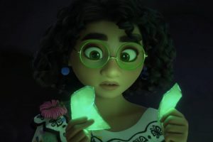 La jeune Encanto observe étonnée un cristal vert fluo qu'elle tient brisé dans ses mains ; scène du film Encanto, la fantastique famille Madrigal pour notre article sur Disney 2021.