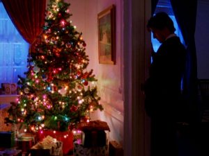 Tom Cruise debout, dans l'embrasure d'une porte plongée dans la pénombre, le visage baissé vers un sapin de Noël lumineux ; plan issu du film Eyes Wide Shut.