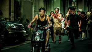 Scène du film The Sadness où un jeune homme tente de fuir en moto un groupe d'infectés dans la rue.