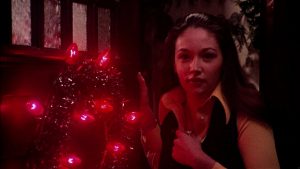 Une des jeunes étudiantes de Black Christmas près d'un sapin de Noël, dont les guirlandes uniquement rouges éclairent toute l'image en clair-obscur.