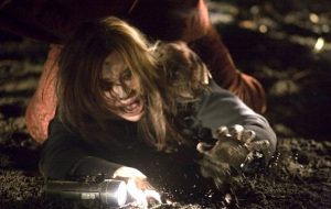 Une jeune femme blonde terrorisée rampe sur le sol de nuit, hurlant, et tentant de saisir la lampe-torche devant elle dans le film Black Christmas (2006).