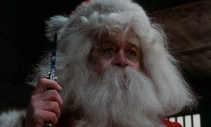 Un vieil homme à l'air épuisé, déguisé en Père Noël, tient un couteau dans la main dans le film Christmas Evil.