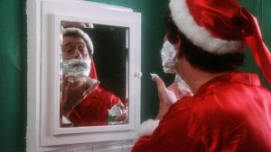 Harry, déguisé en Père Noël, se rase la barbe devant le miroir, sur fond de mur vert, dans le film Christmas Evil.