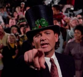 Bill Murray en maître de cérémonie, avec un chapeau haut de forme, tend le doigt vers nous, derrière lui une foule ; scène du film Fantômes en fête.