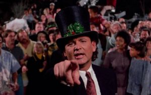 Bill Murray en maître de cérémonie, avec un chapeau haut de forme, tend le doigt vers nous, derrière lui une foule ; scène du film Fantômes en fête.