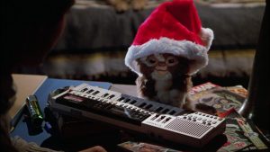 Un petit mogwaï fait du synthétiseur, avec un bonnet du Père Noël sur la tête dans la e film Gremlins.