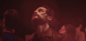 Plan rapproché-épaule sur Kévin Mishel, dans une fête baignée dans une lumière rouge, où il regarde le plafond ; plan issu du film Hors du monde de Marc Fouchard.