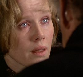 Gros plan sur le visage de Liv Ullmann, les yeux rougis, le regard interrogateur ; face à elle un homme dont nous ne voyons que l'épaule gauche, en amorce ; plan issu du film L'œuf du serpent.