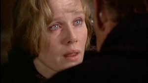 Gros plan sur le visage de Liv Ullmann, les yeux rougis, le regard interrogateur ; face à elle un homme dont nous ne voyons que l'épaule gauche, en amorce ; plan issu du film L'œuf du serpent.