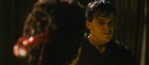 Le tueur du film Black Christmas (2006) perce le crâne d'un homme avec un pic ; nous voyons l'oeil surgir du crâne à gauche, au premier plan, et le visage furieux du tueur à gauche au second plan, de face.
