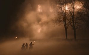 Une maison brûle de nuit, trois silhouettes tentent de s'en approcher dans la fumée, l'une tenant une torche, dans le film Eight for Silver.
