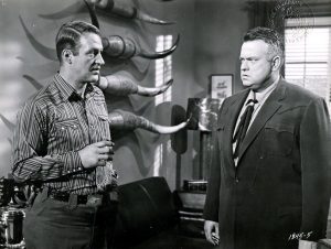 Jeff Chandler et Orson Welles se toisent face à face dans un salon, en fond, des cornes de buffle épinglées au mur tels des trophées de chasse ; plan issu du film Le salaire du diable.
