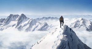 Une silhouette masculine vue de dos contemple un massif montagneux enneigé, au sommet d'un pic ; plan issu du film d'animation Le sommet des dieux.