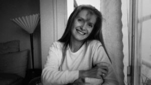 Portrait en noir et blanc de Sophie Toscan Du Plantier souriante, assise près d'une fenêtre, issu du documentaire true crime sur son assassinat proposé par Netflix.