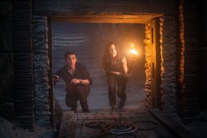 Tom Holland et Sophia Taylor s'apprêtent à entrer dans un tunnel-grotte, accroupis et torche à la main dans le film Uncharted.