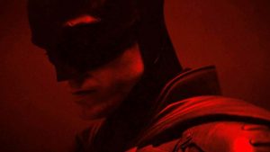 Dans une lumière rouge, Robert Pattinson dans le costume de The Batman, la tête baissée.