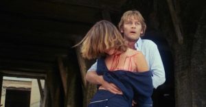 Helmut Berger tient en otage devant lui, en bouclier humain, une jeune femme ensanglantée dont le visage est caché derrière ses cheveux ; plan issu du film Ultime violence.