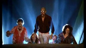 Cinq silhouettes humaines aux yeux brillants de manière surnaturelle gravissent un escalier d'où surgit une lumière bleue pâle fantômatique dans le film Démons.