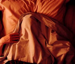 le visage d'une vieille femme, dont nous ne voyons que les mains, est cachée sous un drap blanc, dans un lit ; plan en plongée issu du film Vortex de Gaspar Noé pour notre interview.