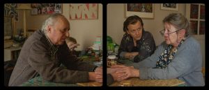 Attablés autour d'une petite table de cuisine vieillotte, Dario Argento, Françoise Lebrun se tiennent les mains, face à face, sous le regard d'Alex Lutz, à côté d'eux ; scène du film Vortex de Gaspar Noé pour notre interview.