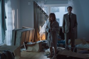Un homme et une femme, quinquagénaires, en costume de ville beige, sont, sonnés, au milieu d'une chambre sans dessus dessous, comme après un cambriolage, dans le film Underdogs.