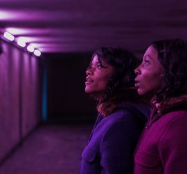 Les deux jumelles du film The Silent Twins sont dans un tunnel éclairé d'une étrange violette, elles observent la paroi sur leur gauche avec admiration.