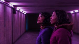 Les deux jumelles du film The Silent Twins sont dans un tunnel éclairé d'une étrange violette, elles observent la paroi sur leur gauche avec admiration.