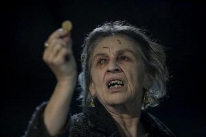 La vieille sorcière effrayante du film Jusqu'en enfer de Sam Raimi regarde étrangement une pièce qu'elle tient dans sa main.