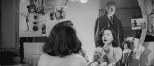 Dans sa loge, une actrice voit dans le miroir pendant qu'elle se démaquille un homme qui s'approche d'elle, d'une allure inquiétante, qui la fixe ; scène du film Les Vampires.
