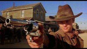 Plan rapproché-épaule sur Leonardo Di Caprio en cow-boy menacant un adversaire avec un revolver dans le film Mort ou vif de Sam Raimi.