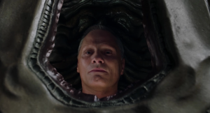 Gros plan du film Les crimes du futur sur le visage de Viggo Mortensen, vu à travers une brèche dont on ne sait si c'est une bouche monstrueuse, ou un tissu. 