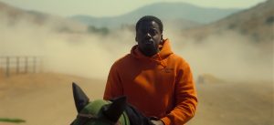Au coeur du désert, Daniel Kaluuya est sur un cheval, les yeux intrigués, il porte étrangement un épais sweat à capuche orange ; plan issu du film Nope.