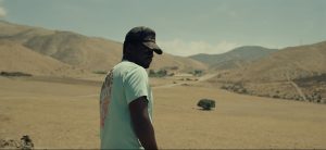 Daniel Kaluuya vu de trois quart, arbore une mine méfiante ; à l'arrière-plan, le désert californien du film Nope.