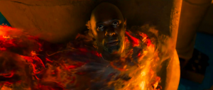 Plan en plongée issu du film Trois mille ans à t'attendre sur Idris Elba, qui semble être englouti par des flammes ; il est torse nu sur un fond doré.