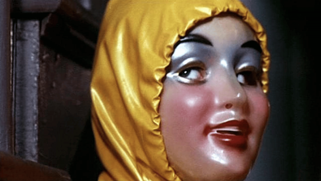 Plan rapprroché-épaule sur ce qui semble être une enfant, portant un masque de femme très maquillée et un ciret jaune ; issu du film Alice sweet Alice.