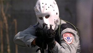 Un braqueur avec un masque blanc de hockey dirige sa mitraillette droit vers nous ; plan issu du film Heat.