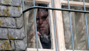 Le visage de Laurent Lucas se dessine à travers la fenêtre d'une vieille maison en pierre et ses barreaux dans le film Calvaire.
