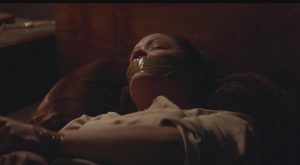 Une femme est allongée dans un lit, les yeux clos, mains liées bâillonnée, dans le film Bowling Saturne de Patricia Mazuy.