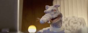Plan rapproché-épaule sur un rat à taille humaine, vêtu de la combinaison bleue et blanche du film Fumer fait tousser.