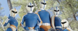 Au cœur d'un bois, les cinq super-héros du film Fumer fait tousser prennent la pose, dans leur combinaison bleue et blanche, le visage casqué, similaires à des Powers Rangers.