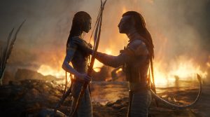 Deux Na'vi, mâle et femelle se font face, sur un fond de nature ravagée par les flammes, comme après une bataille, dans le film Avatar : la voie de l'eau.