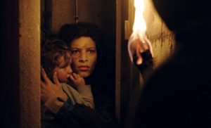 Une torche en flamme révèle une maman et son bébé caché dans ce qui semble être un recoin d'un immeuble désaffecté ; scène du film La tour de Guillaume Nicloux.