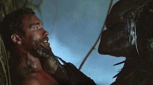 Predator tient Arnold Schwarzenegger par le menton dans un face à face angoissant ; tiré du film Predator de 1987 abordé par le documentaire In search of tomorrow.