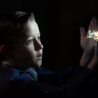 Une petit garçon est fasciné par l'image qui est projetée sur sa main, et qui n'éclaire que son visage au milieu de la pénombre ; plan issu du film The Fabelmans.