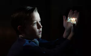 Une petit garçon est fasciné par l'image qui est projetée sur sa main, et qui n'éclaire que son visage au milieu de la pénombre ; plan issu du film The Fabelmans.